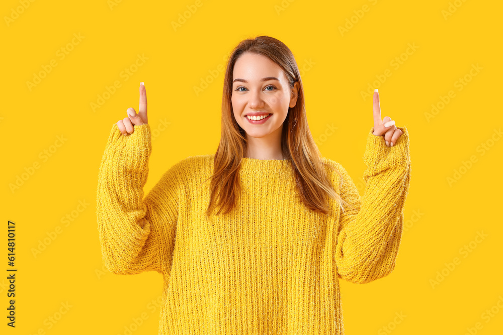 Beautiful young woman pointing at something on yellow background