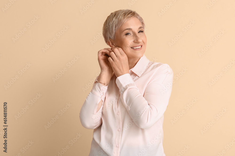 Mature blonde woman with earrings on beige background