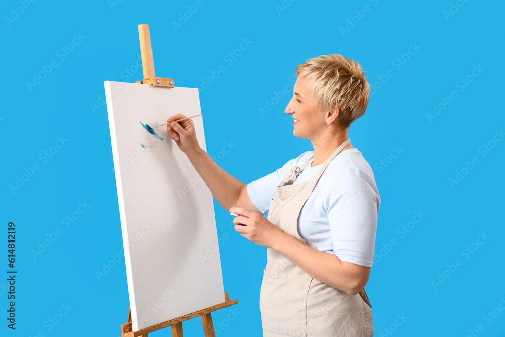 Mature female artist painting picture on blue background