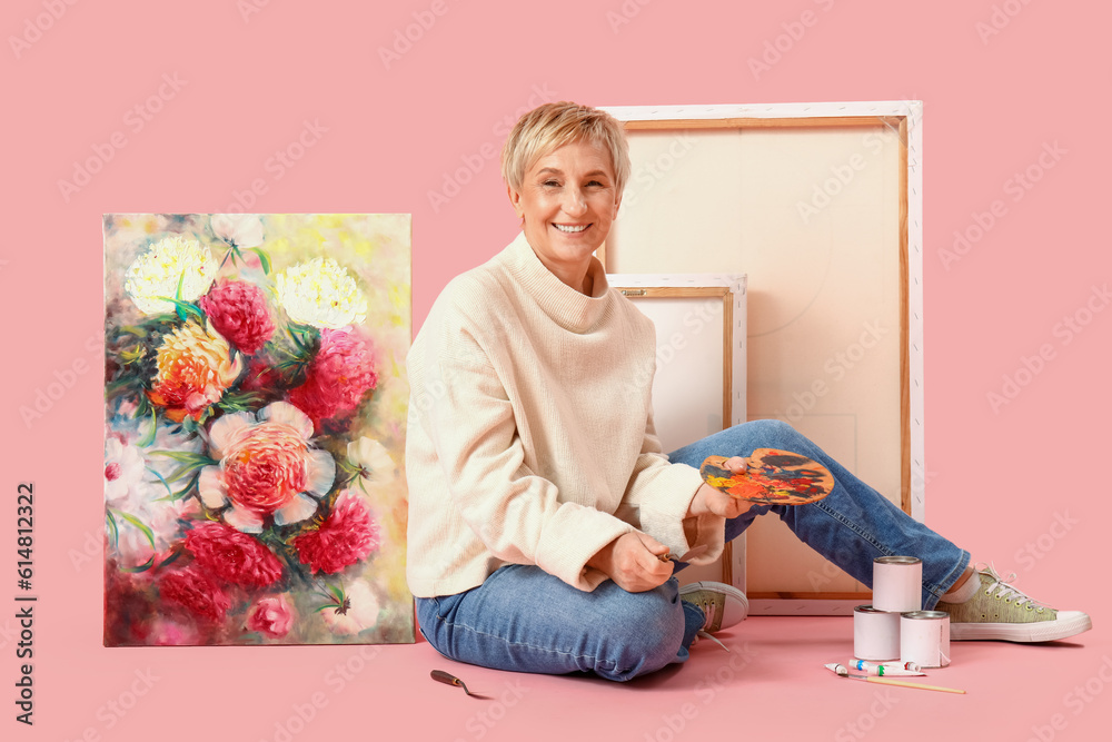 Mature female artist with picture and tools on pink background