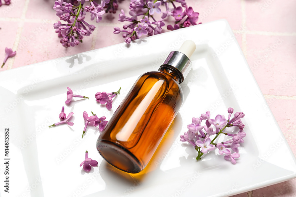 Bottle of lilac essential oil and flowers on pink background, closeup