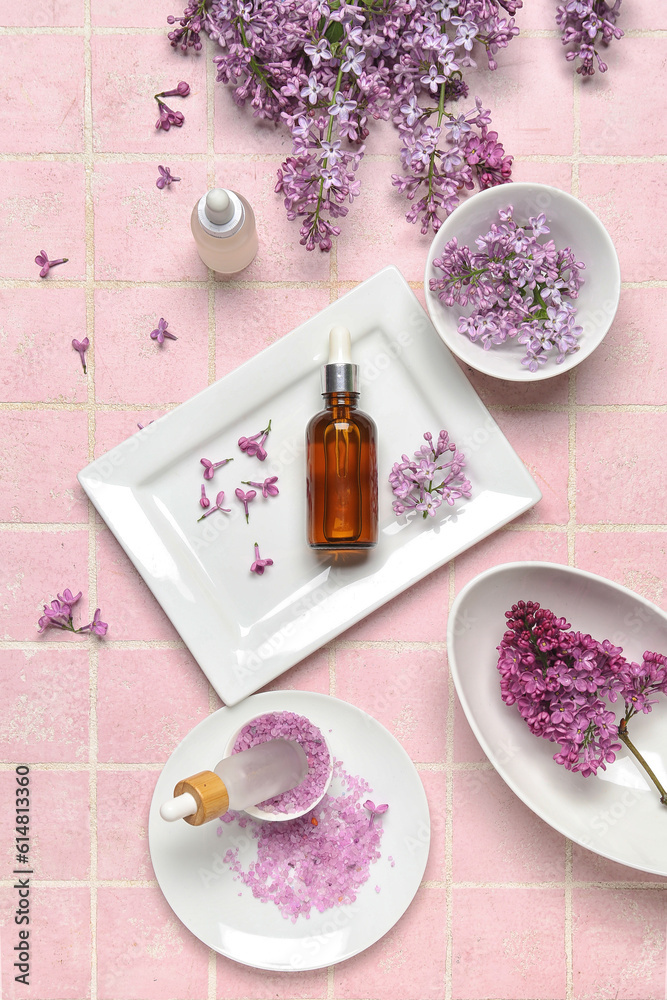 Composition with bottles of lilac essential oil, sea salt and flowers on pink background