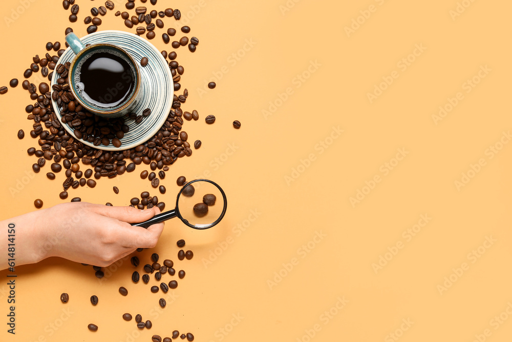 Female hand with magnifier, cup of coffee and beans on pale orange background