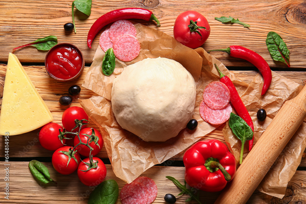 Raw dough and ingredients for preparing pizza on wooden background