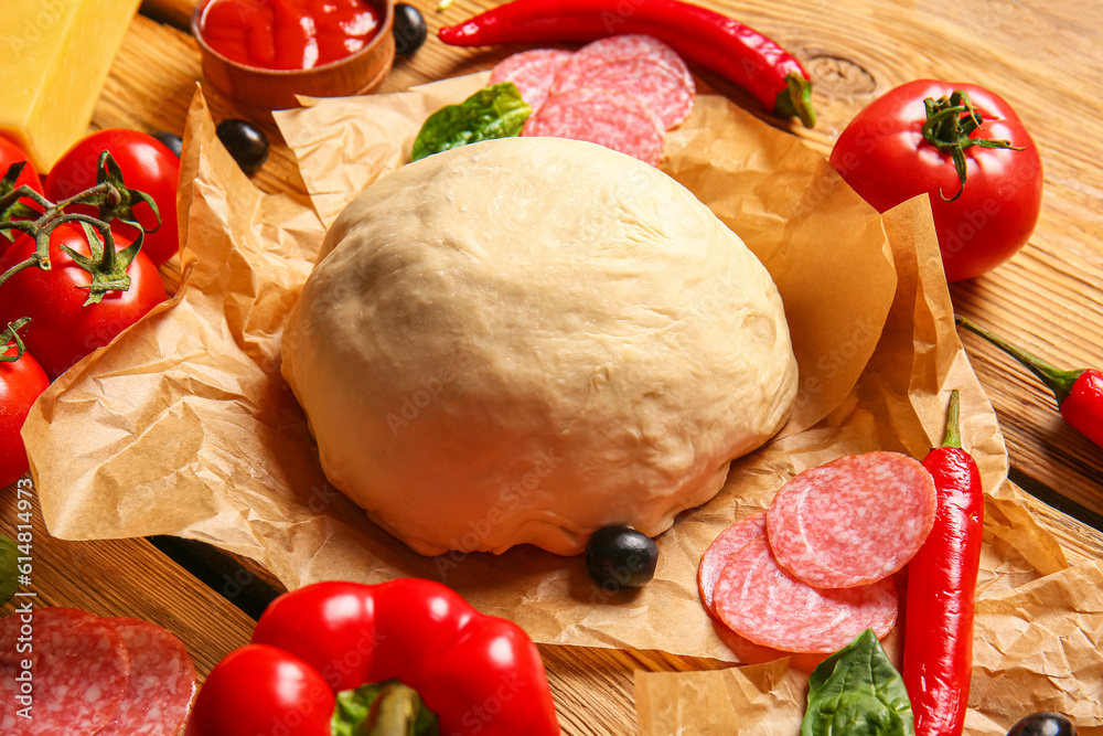 Raw dough and ingredients for preparing pizza on wooden background