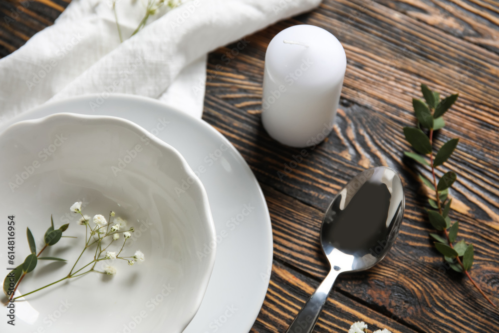 Plates with spoon, flowers and candle on brown wooden background