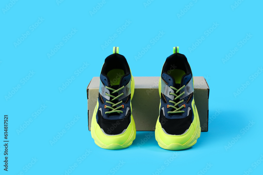 Cardboard box with stylish sneakers on blue background