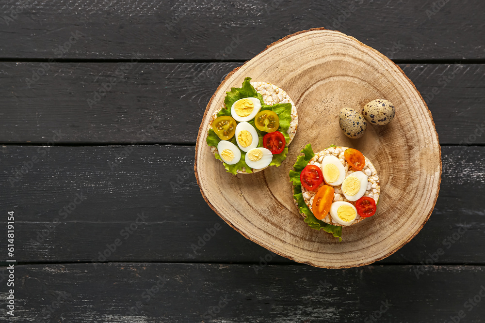 Rice crackers with quail eggs, tomatoes and lettuce on dark wooden background