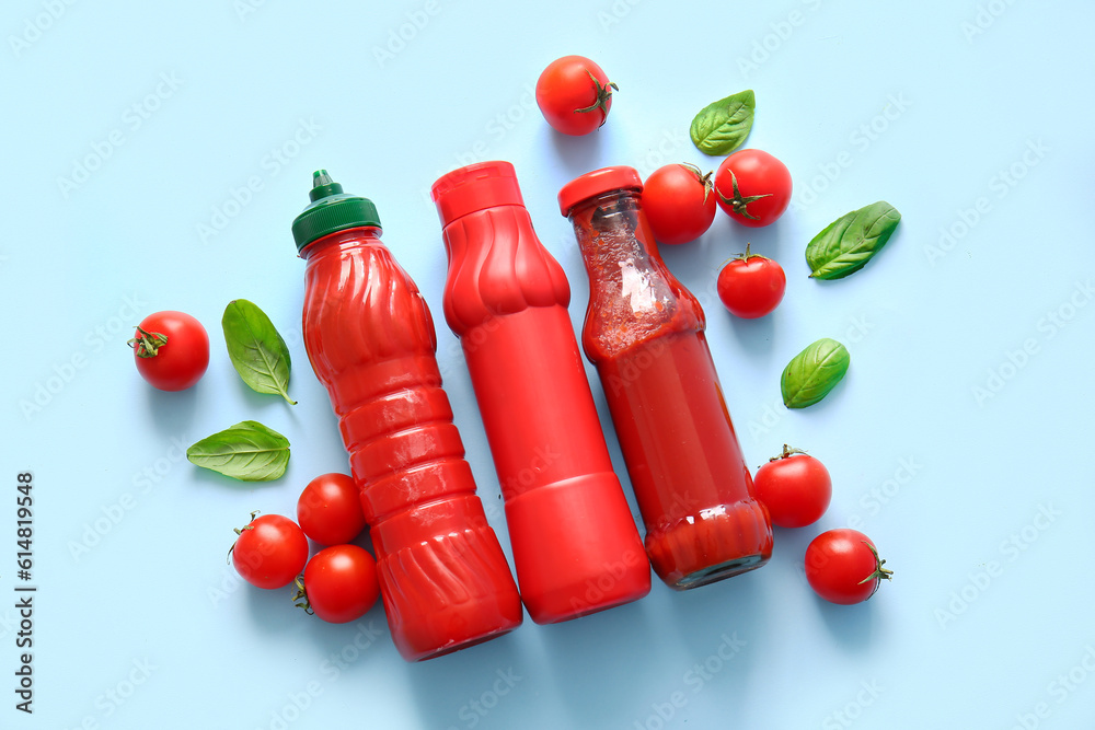 Bottles of ketchup and tomatoes on blue background