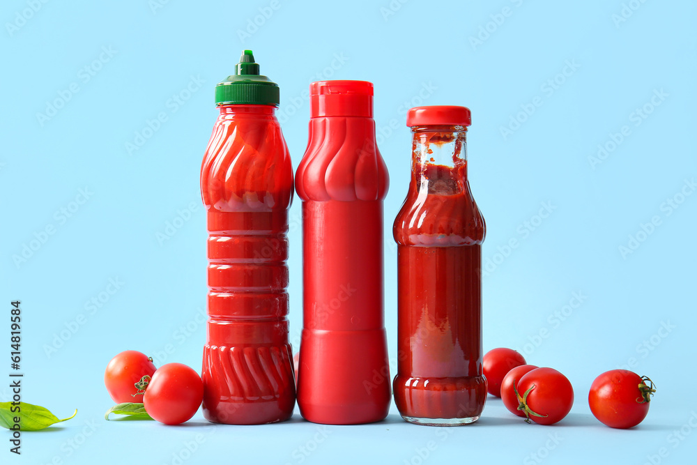 Bottles of ketchup and tomatoes on blue background