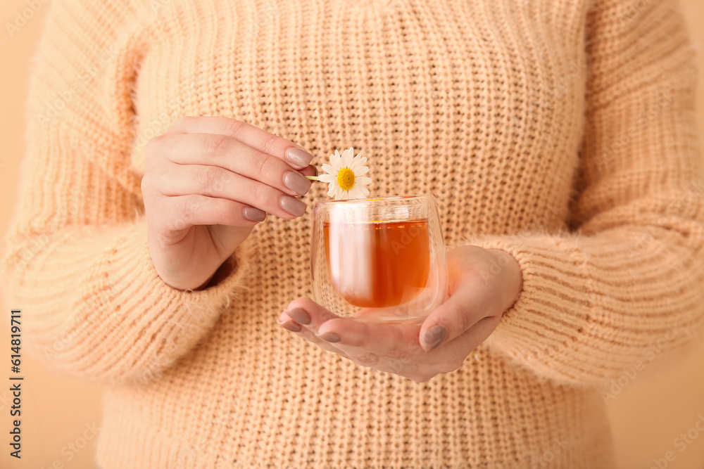 Beautiful young woman with cup of chamomile tea near beige wall