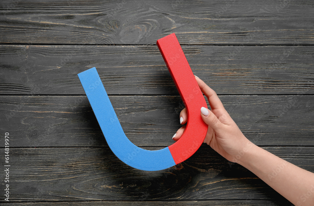 Female hand with magnet on dark wooden background