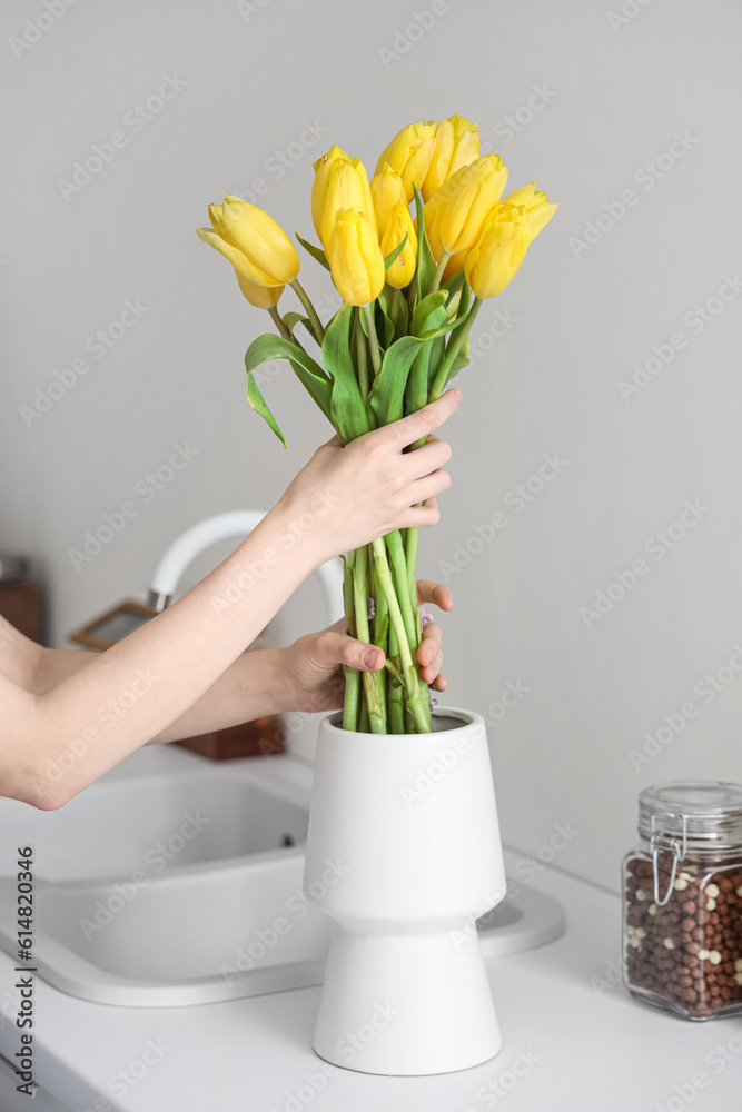 Woman taking bouquet of yellow tulip flowers from vase on white kitchen counter