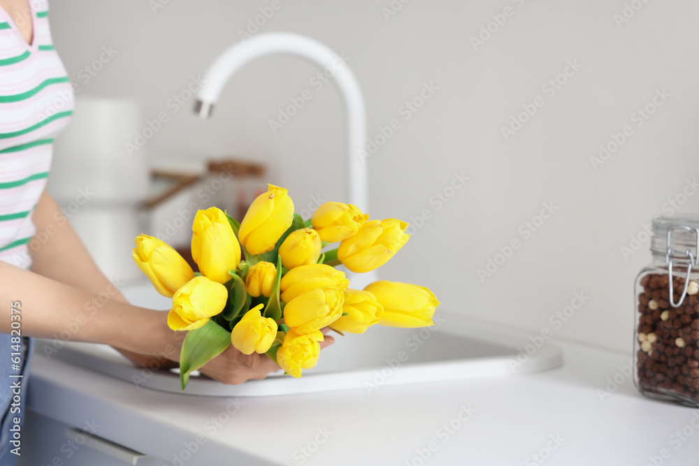 Woman holding bouquet of yellow tulip flowers near kitchen sink