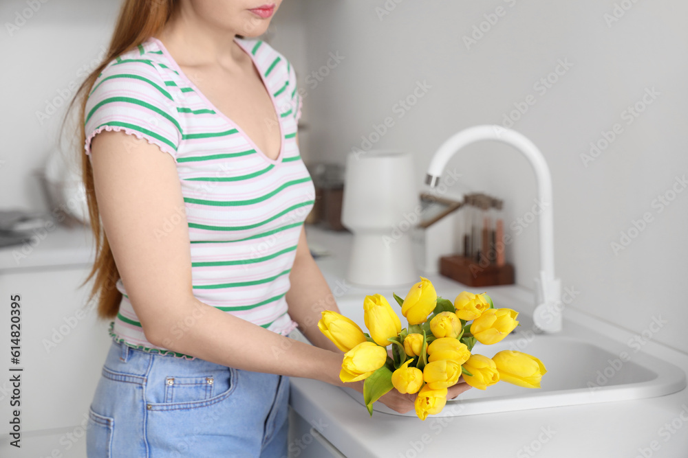 Woman holding bouquet of yellow tulip flowers near kitchen sink