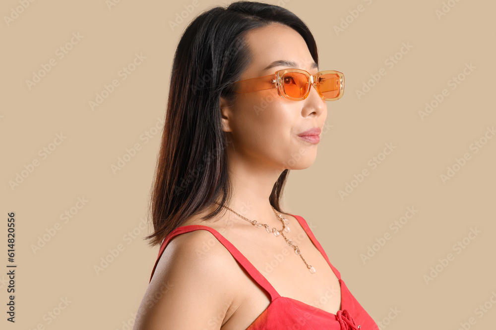 Beautiful Asian woman in stylish sunglasses on beige background, closeup