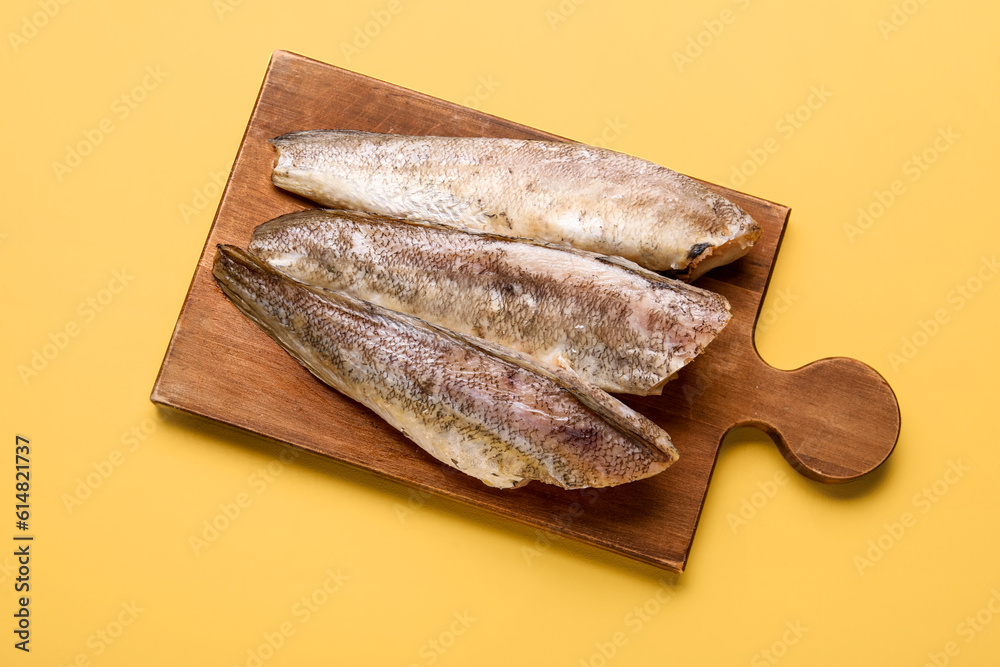 Wooden board with raw codfish on yellow background