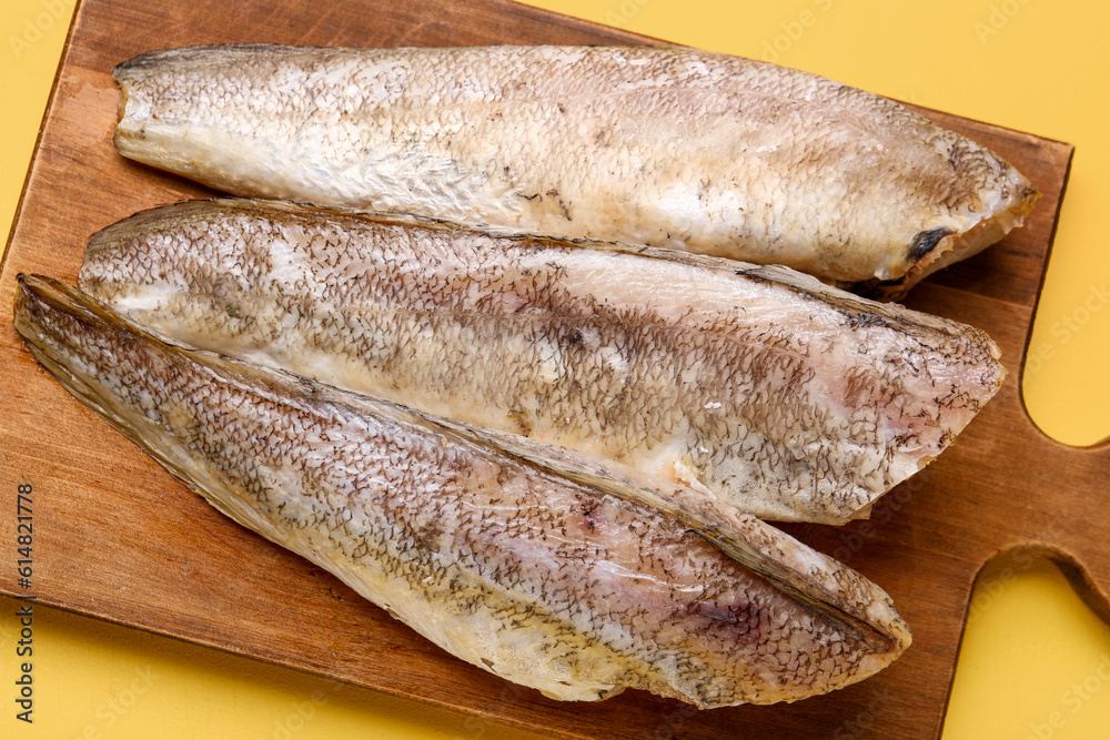 Wooden board with raw codfish on yellow background