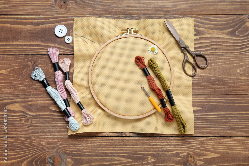 Embroidery hoop with canvas, scissors and mouline threads on brown wooden background