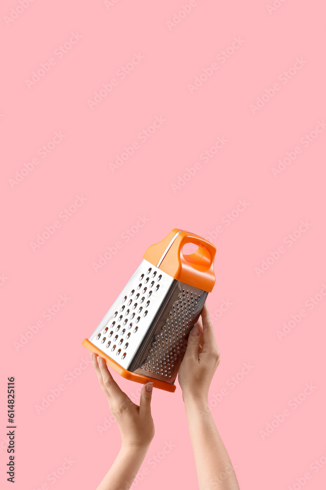 Female hands holding grater on pink background