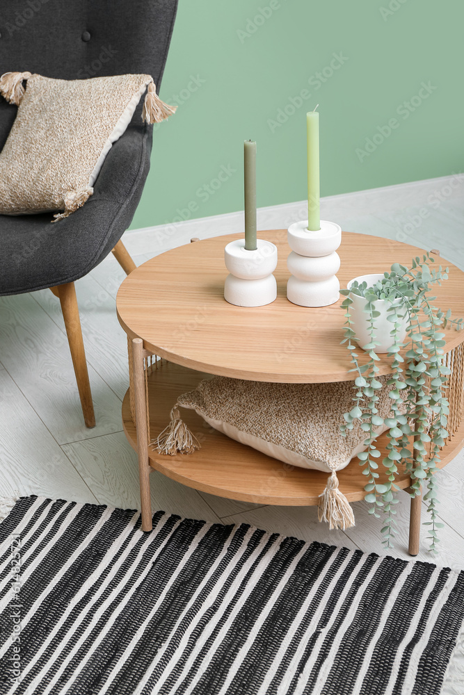 Stylish interior of living room with armchair, table, candles and soft rug