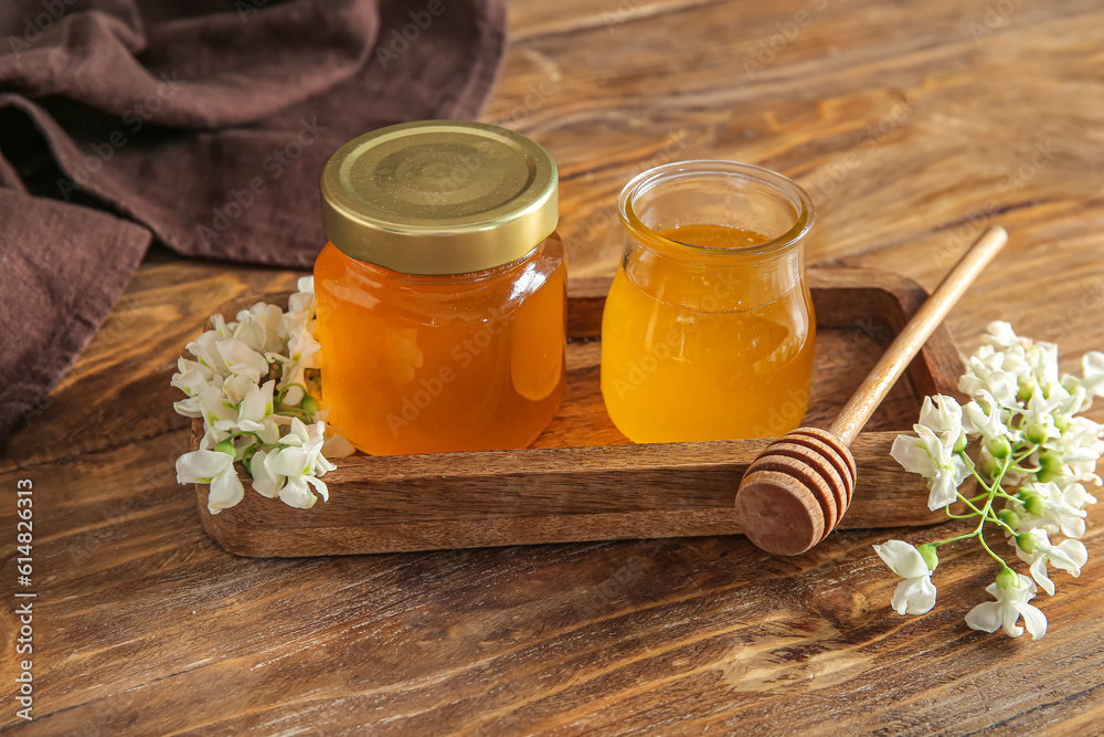 Jars of honey with flowers of acacia on wooden background, closeup