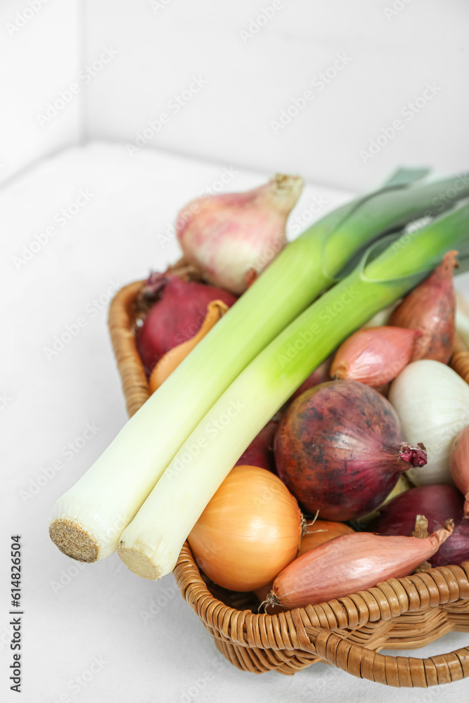 Wicker basket with different kinds of onion on light background, closeup