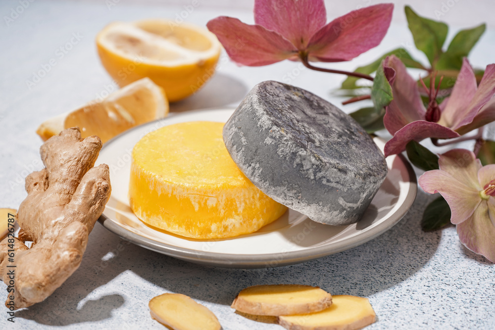 Different handmade solid shampoo, orchid flowers, lemon and ginger on light background, closeup