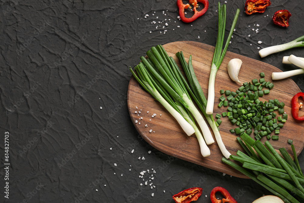 Board with slices of fresh green onion and pepper on black background