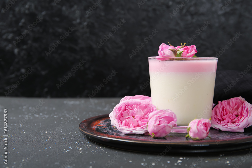 Glass of panna cotta with beautiful pink rose flowers on black table