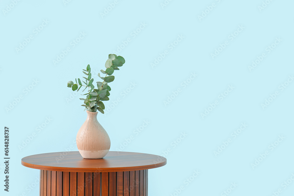 Wooden coffee table with eucalyptus branches in vase near blue wall