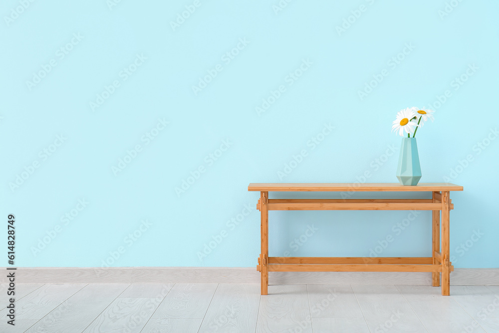 Wooden table with blooming daisy flowers in vase near blue wall