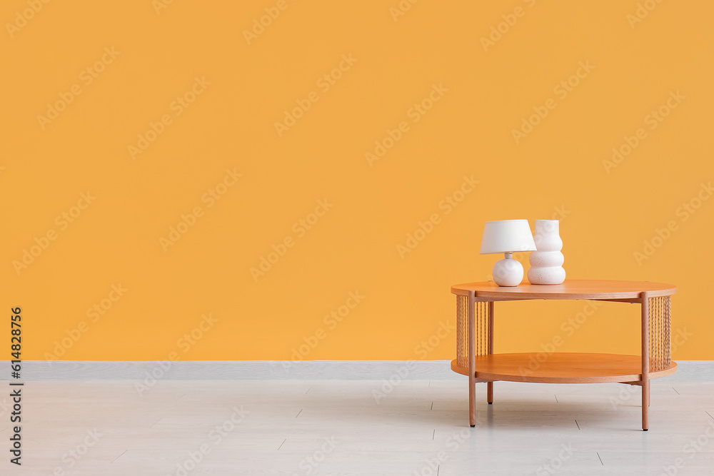 Wooden coffee table with lamp and empty vase near orange wall