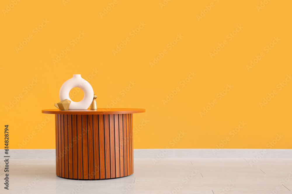 Wooden coffee table with empty vase and decorative figures near orange wall