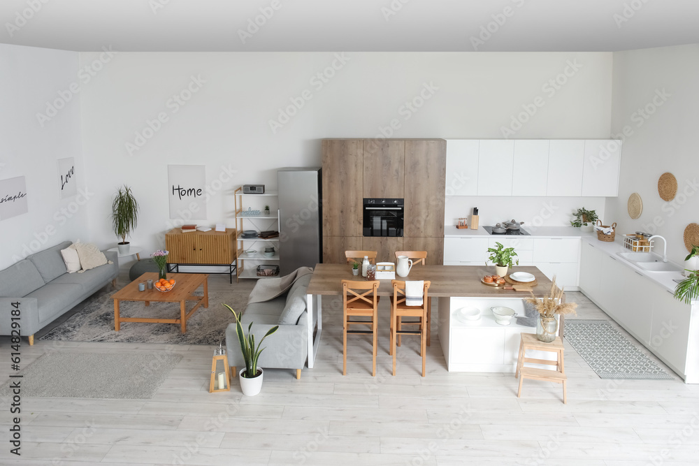 Interior of light open plan kitchen with island table and grey sofas