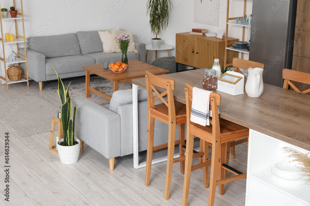 Interior of light open plan kitchen with island table and grey sofas