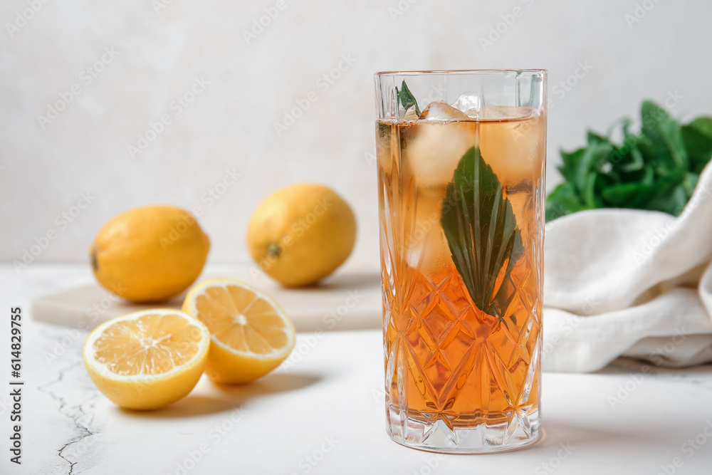 Glass of ice tea and board with lemons on white background