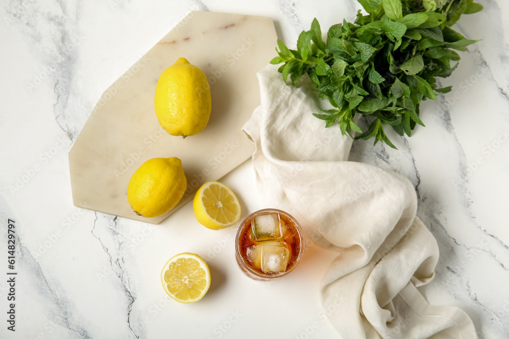 Glass of ice tea and board with lemons on white background