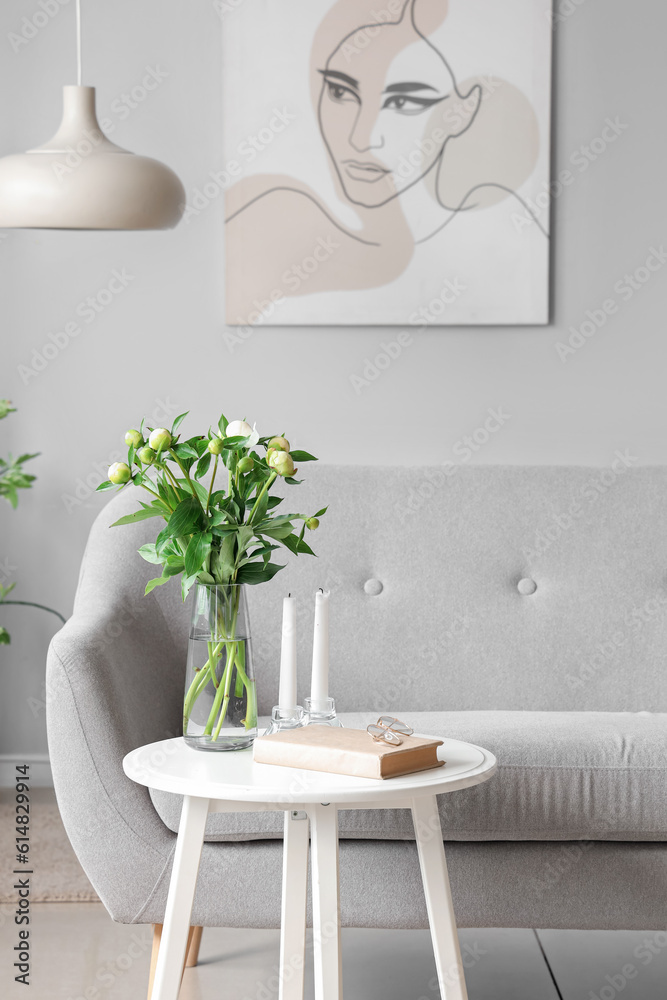 Vase with unopened peonies, candles and eyeglasses in living room