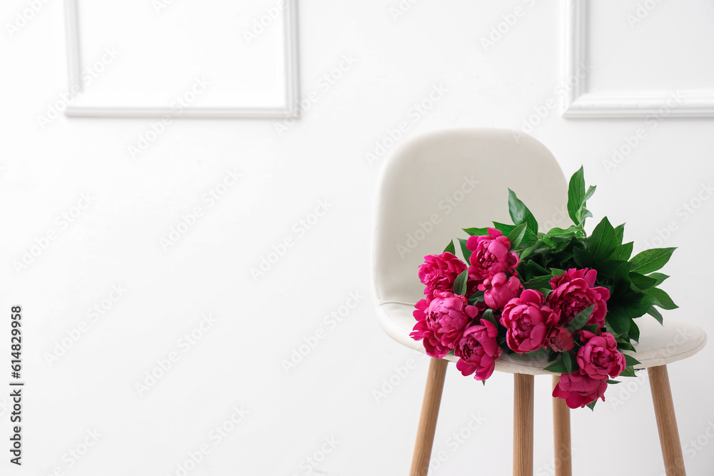 Bouquet of peonies on chair near white wall