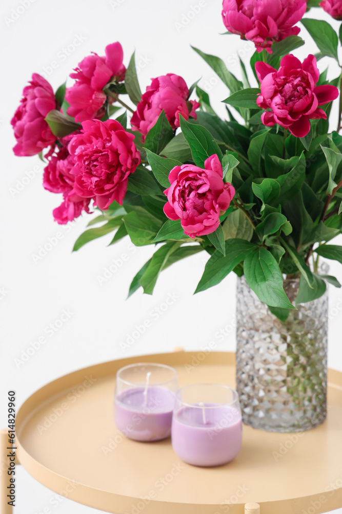 Vase with red peonies and candles on coffee table near white wall