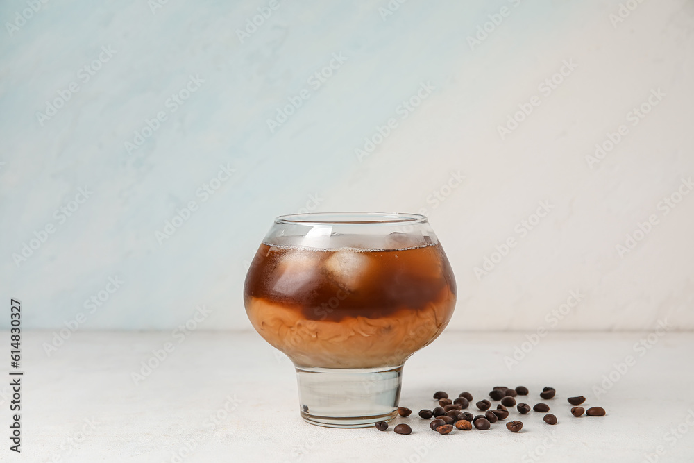 Glass of tasty ice coffee with milk on light background