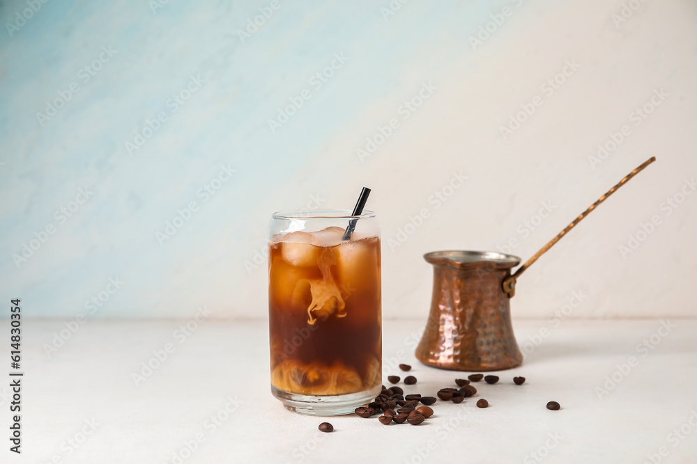 Glass of tasty ice coffee with milk and cezve on light background