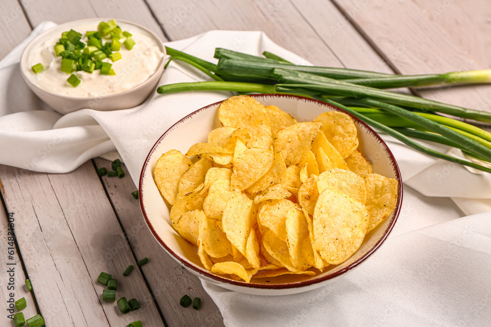 Bowl of tasty sour cream with sliced green onion and potato chips on grey wooden background