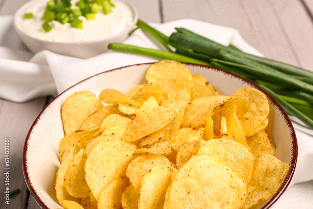 Bowl of tasty sour cream with sliced green onion and potato chips on grey wooden background