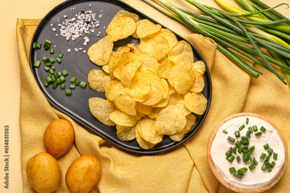 Bowl of tasty sour cream with sliced green onion and potato chips on yellow background