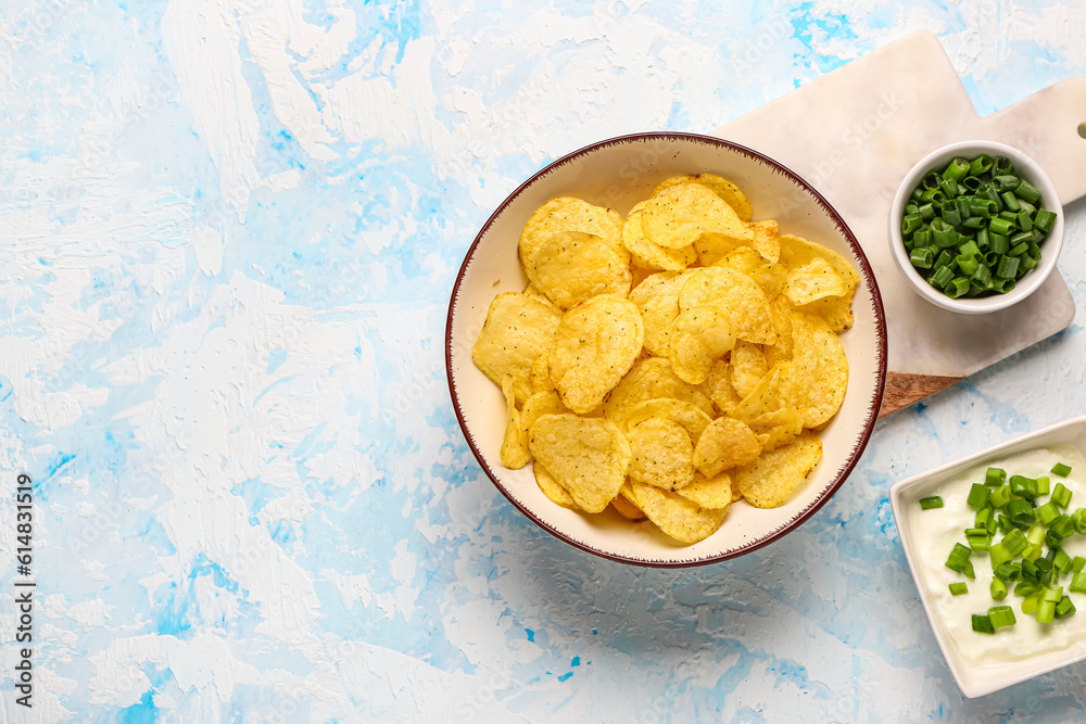 Bowls of tasty sour cream with sliced green onion and potato chips on blue background