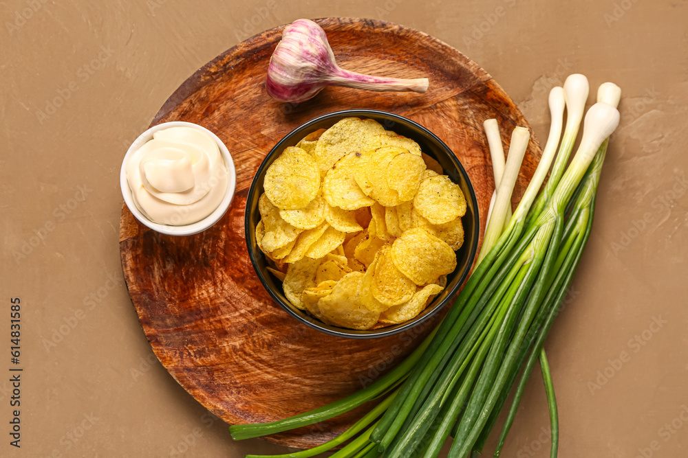 Bowl of tasty sour cream with green onion and potato chips on brown background