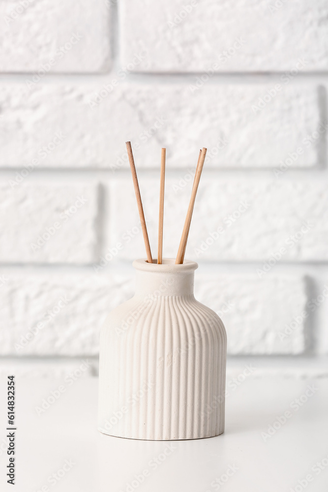 Bottle of reed diffuser on table near light brick wall in room, closeup