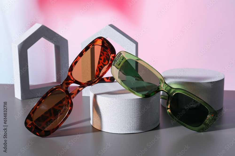 Podiums with different stylish sunglasses on colorful background